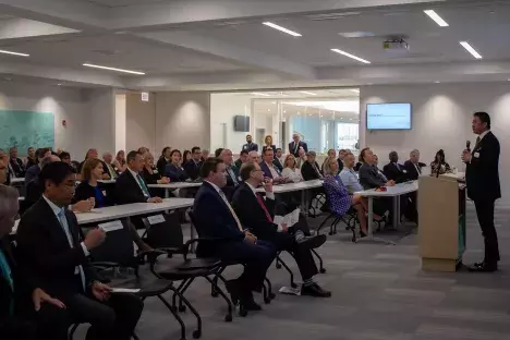 Photo of a large lecture room filled with people while Dr. Nakao stands at the podium giving a speech